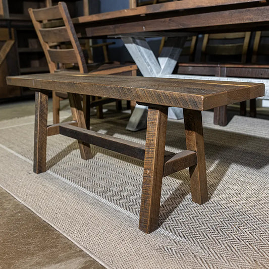Rustic solid wood bench with splayed legs and a crossbar on a textured rug.