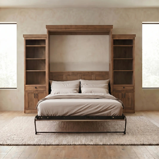 Bed with beige linens, built-in bookcases, light walls, wood floors, and two large windows.