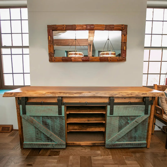 Barnwood buffet with walnut top and steel hardware under mirror, flanked by tall windows.