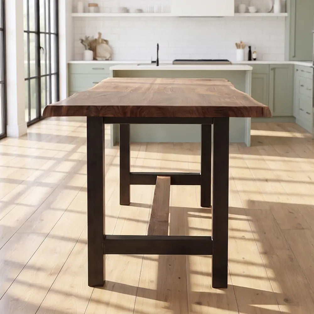 Walnut counter table with steel base in a bright kitchen with sage cabinets and large windows.