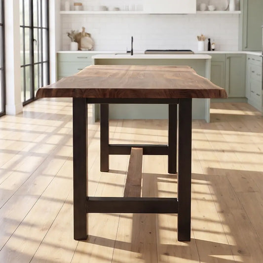 Walnut counter table with steel base in a bright kitchen with sage cabinets and large windows.