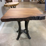 A 25" Live Edge Sycamore End Table featuring a small square steel base, black metal legs, and a sycamore wood top with live edges, finished in smooth polyurethane and displayed indoors on a polished concrete floor.