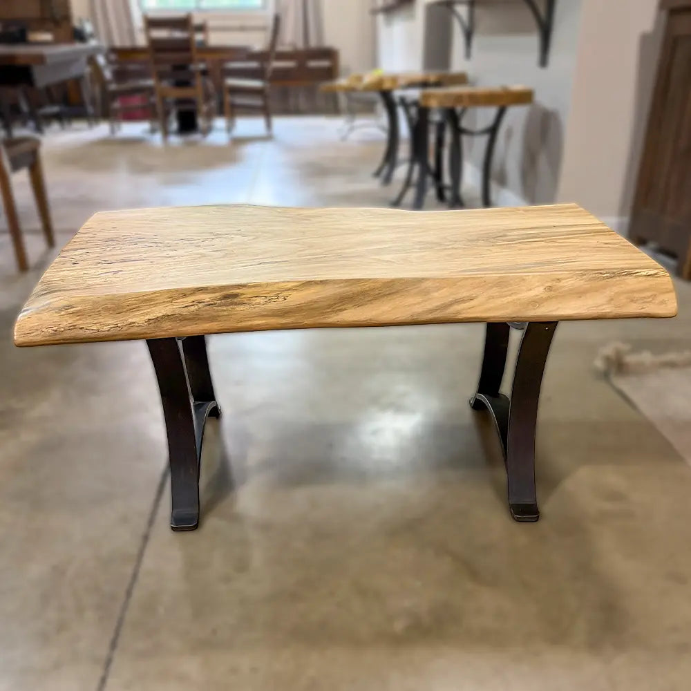 Spalted maple live edge coffee table with black metal legs on concrete floor in showroom.