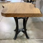 Live edge sycamore end table with black legs on a concrete floor in an indoor setting.