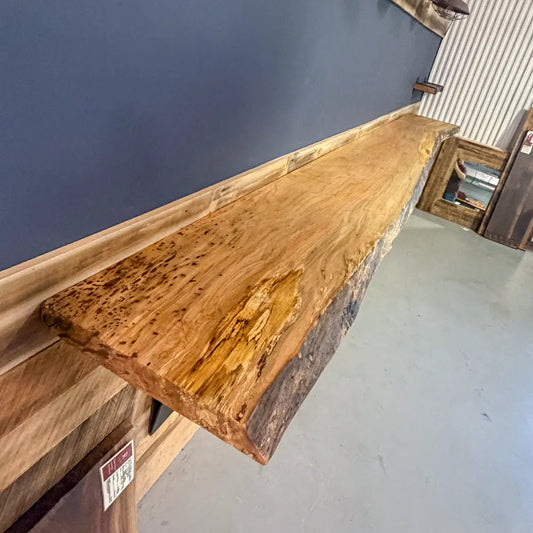 Maple slab bar top with live edge mounted on blue wall, highlighting natural grain and shape.