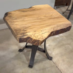Live Edge Sycamore End Table with black steel base on concrete floor by a light wall.